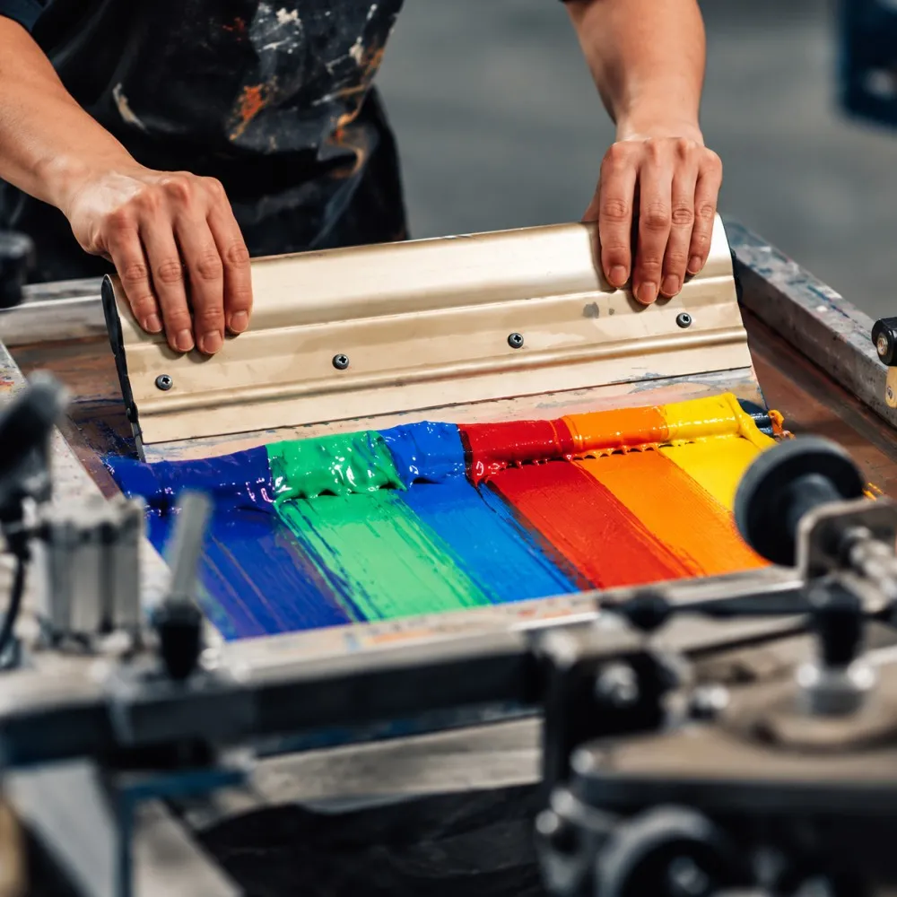 Worker applying colorful ink during the screen printing process.
