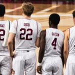 Four basketball players wearing white custom basketball jerseys featuring different player names and numbers on the back while standing on the court.